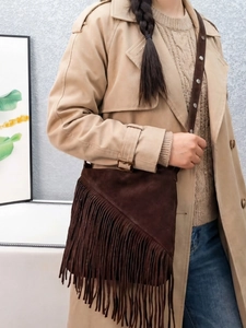 Vintage dark brown suede fringe bucket bag with adjustable rivet strap worn over a coat