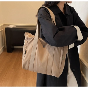 Close-up of beige nylon tote bag with wide shoulder strap and cute bear charm detail