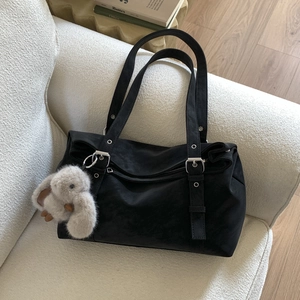 Close-up of black matte shoulder bag with silver hardware and plush bunny charm on sofa