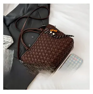 Detailed close-up of dark brown woven bucket bag with wood bead tassel on white fabric