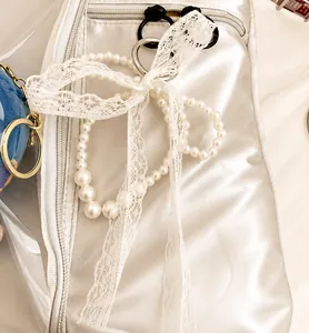 Close-up of white satin bag featuring pearl beads, lace bow, and blue plush pendant charm