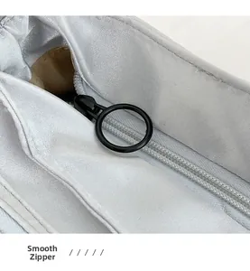 Close-up of a smooth black metal circular zipper on a light gray fabric shoulder bag