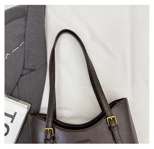 Close-up of dark brown leather tote bag with gold metal buckles and slim shoulder straps