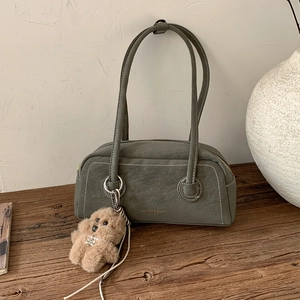 Detail of dark green vintage leather shoulder bag with plush dog charm on wooden desk