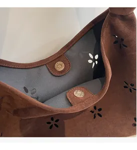 Detail of brown suede tote bag with laser-cut flower patterns and golden magnetic closure