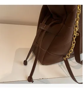 Detail of a brown bucket bag showing the drawstring closure and gold metal chain strap