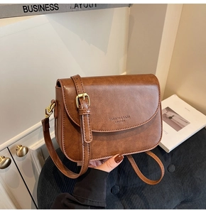 Detail of a brown faux leather crossbody bag with fashion logo and golden metal buckles