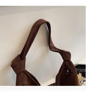 Detail of wide suede handle with knot design and laser-cut floral patterns on the bag