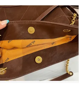 Detail of dark brown quilted leather bag with magnetic closure and orange lining
