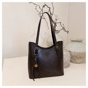 Detail of dark brown tote bag with vintage texture, gold buckle, and woven tassel charm