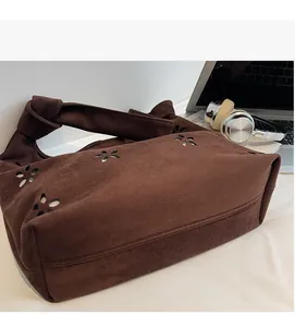 Close-up of brown suede tote bag featuring intricate laser-cut patterns and knotted strap