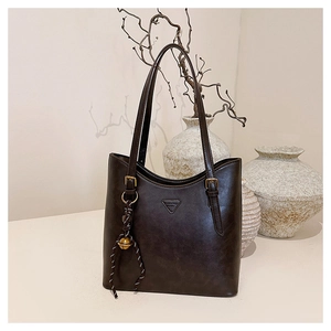 Detail of dark brown oil-wax leather tote bag with vintage finish and side bell charm