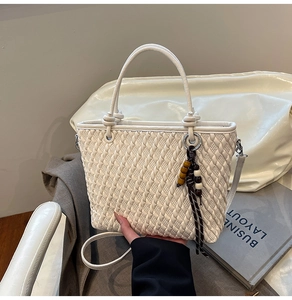 Detail view of cream bucket bag showing woven texture, round handle and beaded charm