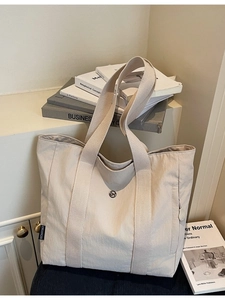 Minimalist off-white canvas tote bag featuring a black brand label and wide woven handles