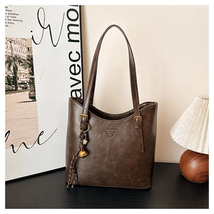 Detailed view of brown leather tote bag featuring a metal logo and woven bell pendant