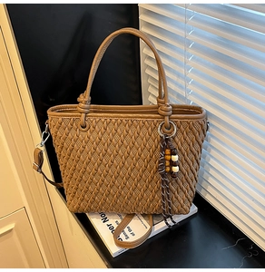 Detail of woven brown bucket bag with beaded tassel charm and adjustable shoulder strap