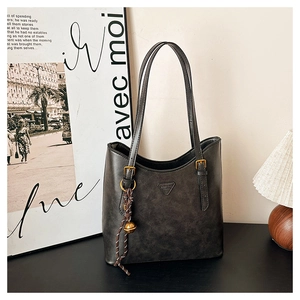 Detail of dark grey tote bag with gold hardware and beaded bell charm accessory