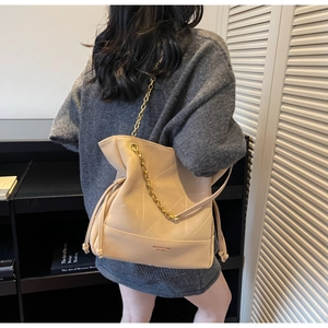 Beige leather bucket bag with gold chain strap shown on model in a cozy interior