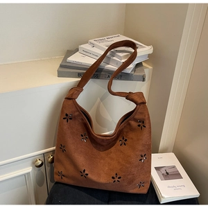 Detail of suede tote bag featuring hollowed floral patterns and a knotted shoulder strap