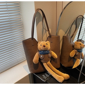 Detailansicht der braunen Leder-Tote-Bag mit einem langbeinigen Plüsch-Teddybären-Anhänger