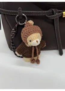 Detail of cute plush bear charm with knit sweater hanging on a brown leather shoulder bag