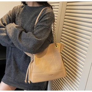 Detail of geometric stitched suede bucket bag with gold chain and brand logo imprint