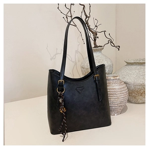 Detail of black leather tote bag featuring a triangle tag and stylish braided pendant