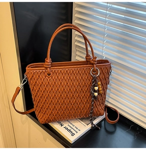 Detail of a brown woven tote bag with knotted handle and beaded charm on a windowsill