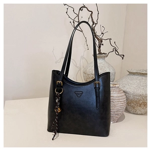 Detail of black faux leather tote bag featuring a woven pendant and a gold bell charm