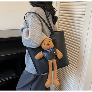 Detail of black faux leather tote bag with cute teddy bear charm in a lifestyle setting