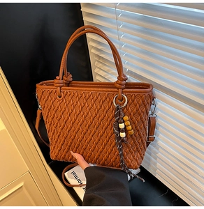 Detail of woven texture tote bag in caramel brown with decorative beaded tassel