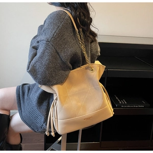 Close-up of beige tote bag with geometric stitching and gold chain strap on model