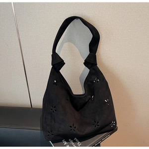 Close-up of laser-cut floral patterns and knotted strap on a black suede underarm bag
