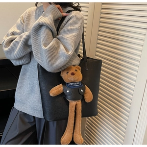 Close-up of black leather bucket bag with cute long-legged teddy bear mascot pendant