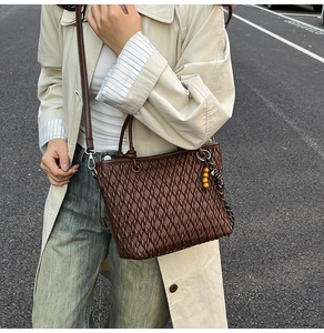 Detail of dark brown tote bag with woven texture and a wooden bead decorative pendant