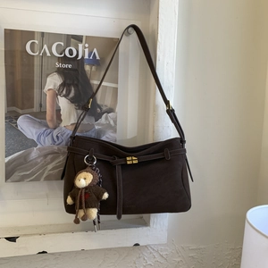 Detail view of brown suede tote bag featuring a leather strap and a cute bear plush charm