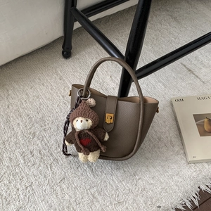 Detail of dark brown leather bucket bag with cute bear charm on a soft white faux fur rug