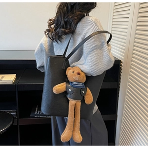 Close-up of black leather tote bag featuring a cute brown teddy bear plush charm