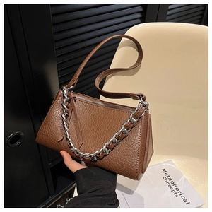 Detail of a brown textured shoulder bag with silver chain strap shown in a modern interior