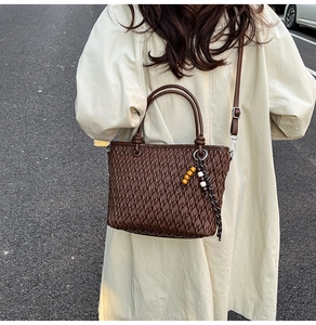 Detail of dark brown bucket bag with quilted texture and beaded charm on beige coat