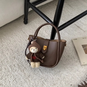 Close-up of brown pebbled leather bucket bag with gold clasp and a cute teddy bear charm