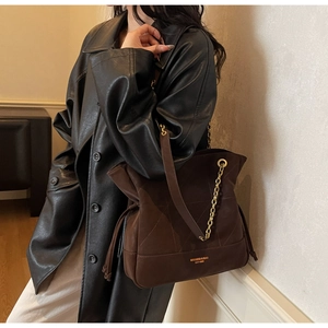 Brown suede bucket bag with gold chain strap shown on a model in a black leather coat