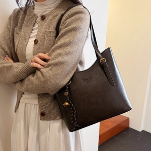 Detail of vintage brown tote bag featuring a triangle logo plaque and braided charm