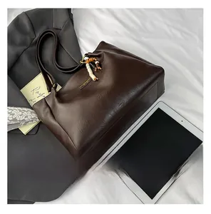 Détail d'un grand sac fourre-tout marron avec texture cuir, pompons et logo métallique