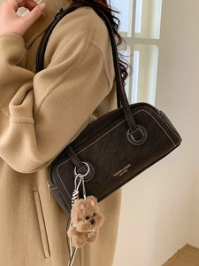 Retro dark brown underarm bag with white stitching and plush bear charm on camel coat