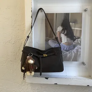 Dark brown suede hobo bag with gold buckle and a bear charm on a white wall