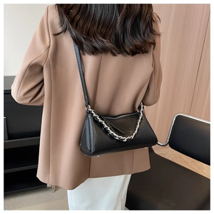 Rear view of model wearing a black textured leather bag with silver chain and thin strap
