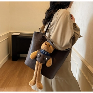 Detail of coffee brown leather tote bag with a cute teddy bear charm on shoulder