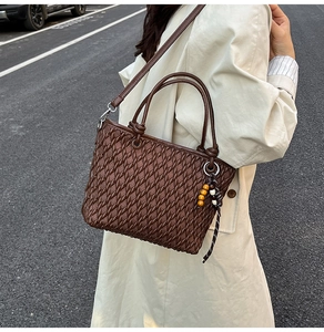 Close-up of deep brown woven bucket bag with wood bead charm and textured leather detail
