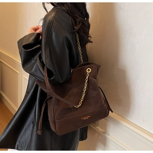 Detail of vintage brown suede bucket bag with gold lettering and metal chain strap